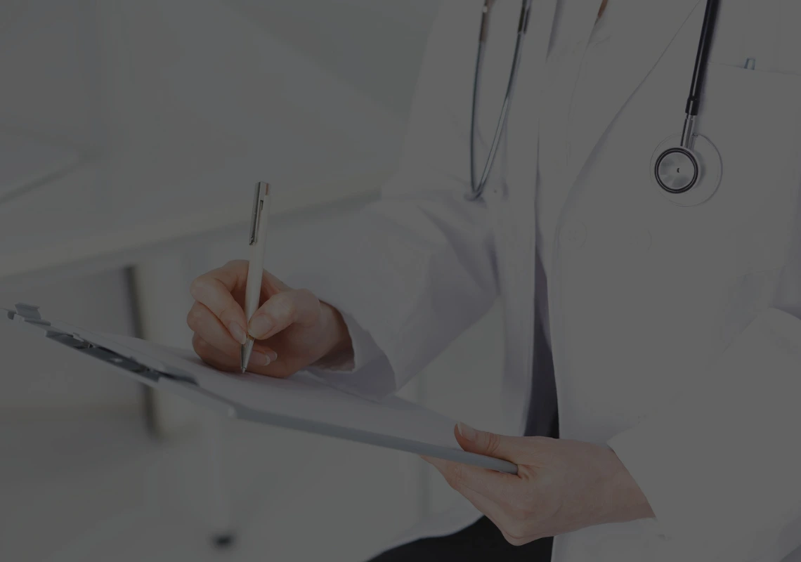 Un profesional sanitario escribiendo sobre un portapapeles. La ia agéntica transforma este tipo de texto libre no estructurado en datos clínicos homogéneos y trazables.
