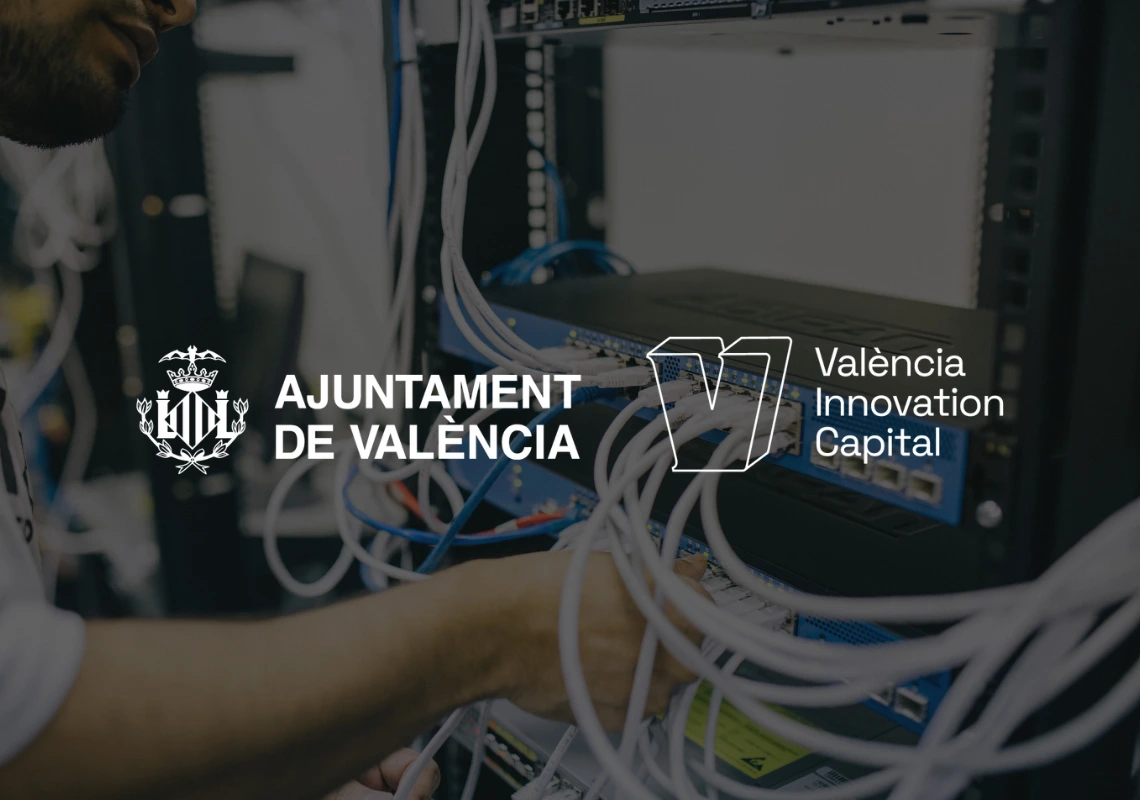 Close-up of a technician working on network server cabling, with the ajuntament de valència and valència innovation capital logos overlaid, representing the technological infrastructure that supports an ai assistant.